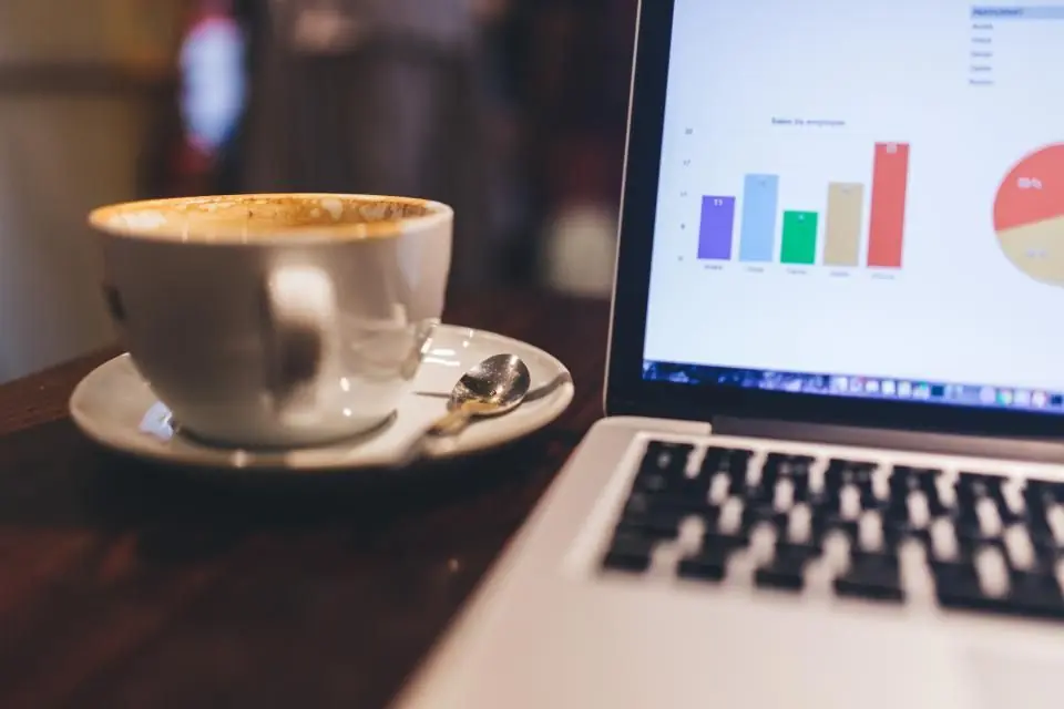 Laptop mit Kostenübersicht neben einer Tasse Kaffee